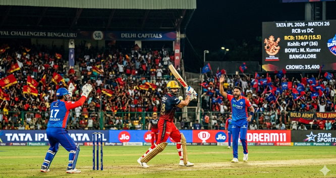 A realistic action shot from the RCB vs DC IPL 2026 Match 26 at a packed M Chinnaswamy Stadium. The image shows a Royal Challengers Bengaluru batter poised at the crease, facing an appeal from the Delhi Capitals wicket-keeper and bowler. The stadium's digital scoreboard clearly displays the match details in the background, making this an authentic visual for cricket preview articles and match updates.